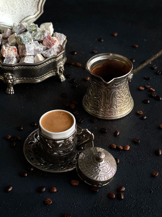 Turkish coffee in a small cup with an ornate cezve and Turkish Delight