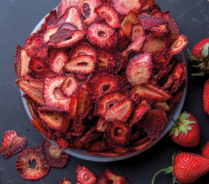 Dried strawberry slices in a bowl with fresh strawberries beside them
