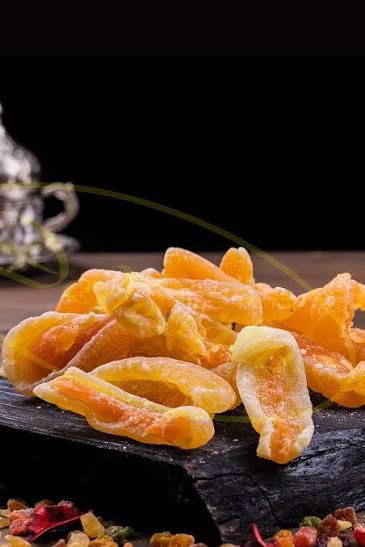 Orange dried melon slices arranged on a dark stone platter against a black background