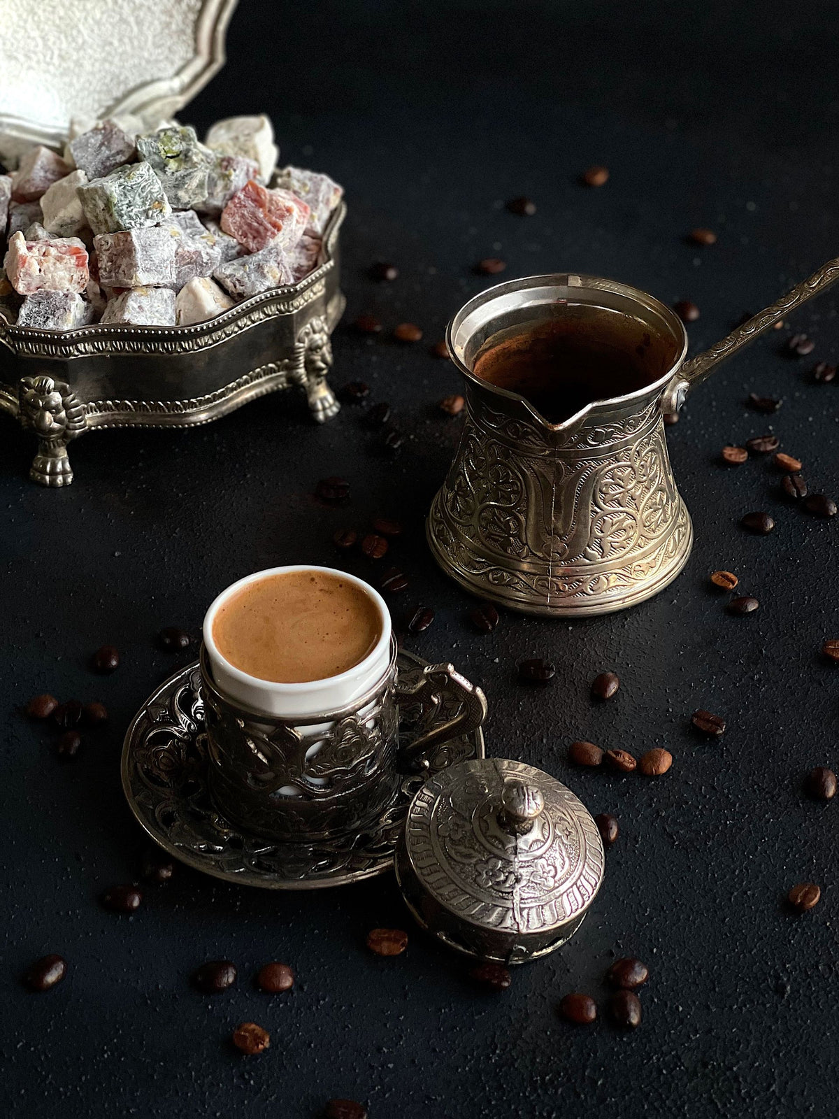 Turkish coffee in a small cup with an ornate cezve and Turkish Delight
