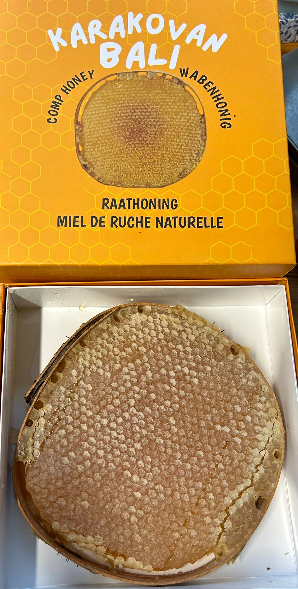 Open orange Karakovan Balı box containing a round honeycomb with the printed lid above