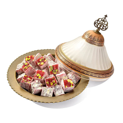 Pink Turkish Delight cubes with visible pistachios and powdered sugar on a gold plate beside a decorative lid