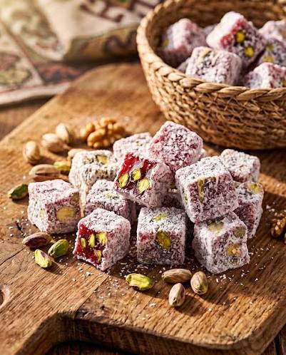 Pink Turkish Delight cubes coated with coconut and topped with visible pistachios on a wooden table
