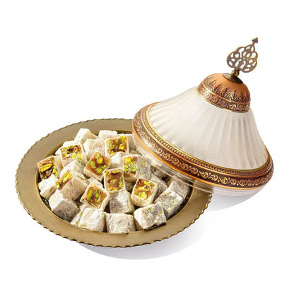 Light-coloured Turkish Delight cubes with visible pistachios and powdered sugar on a gold plate beside a decorative lid
