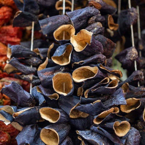 Hollow dried aubergines hanging on strings, showing dark outer skins and pale interiors